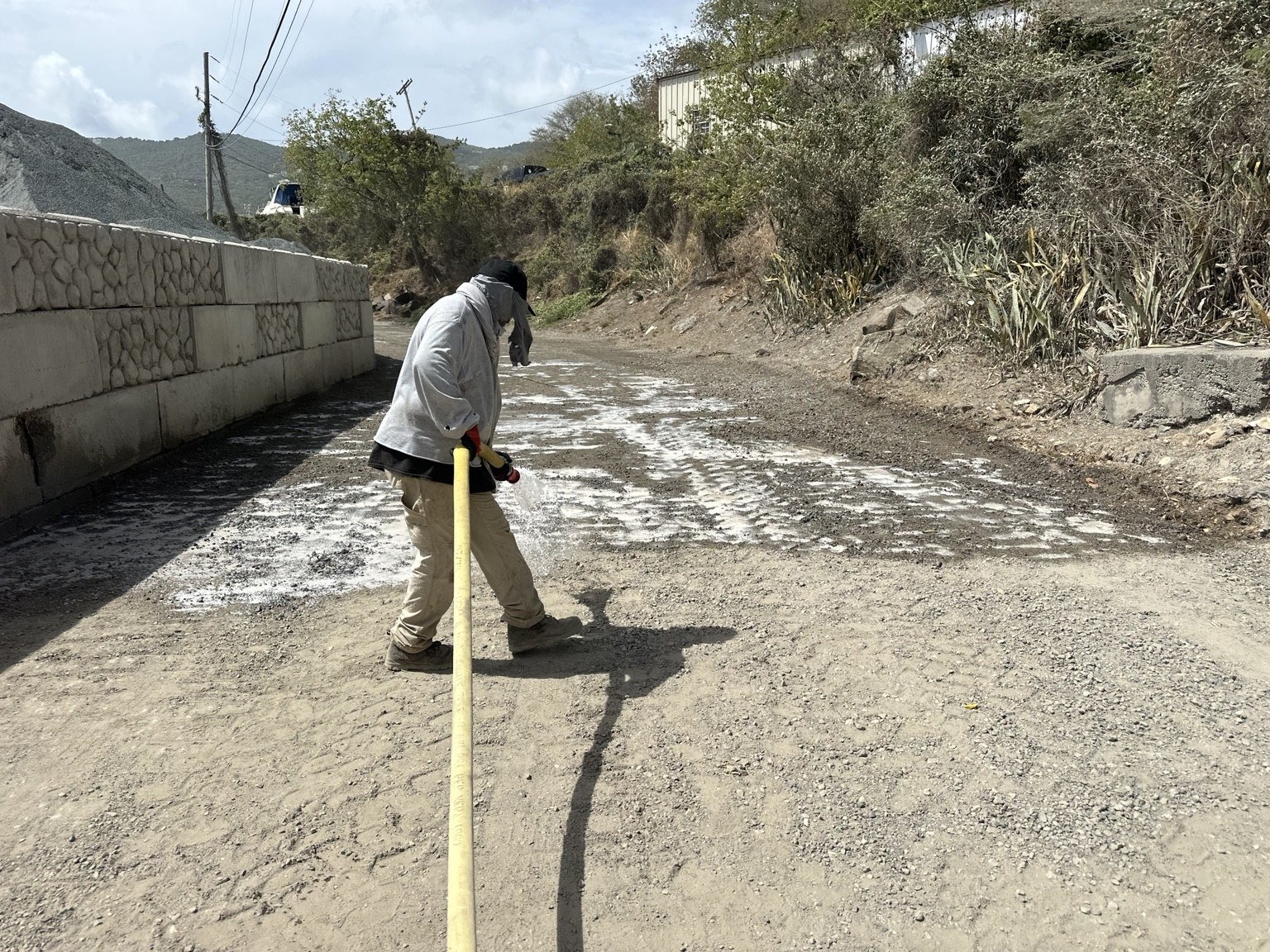 Worker using a hose to spread Solid Earth across a heavy-truck access road in St. Thomas